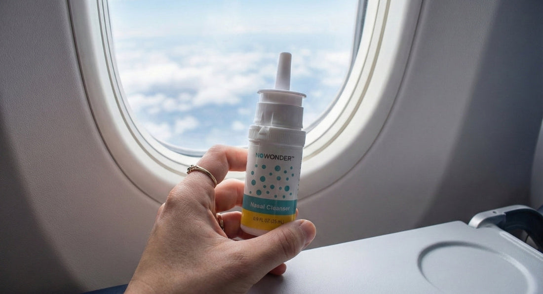A hand holds a bottle of NoWonder Nasal Cleanser next to an airplane window, with clouds visible outside.